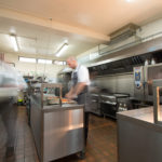 two chefs working in a large kitchen with lots of chrome