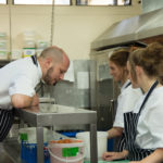 a chef standing over the pass talking to two younger chefs