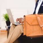 man sat with leather bag on apple mac