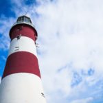 a red and white lighthouse with wisps of clouds and blue sky