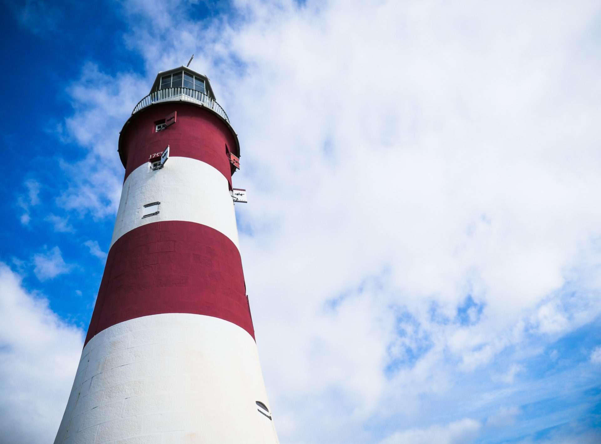 a red and white lighthouse with wisps of clouds and blue sky