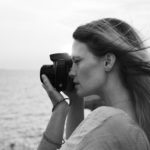 lady by the sea with a camera taking a picture